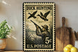 A vintage-style stamp depicting a man hunting ducks, with the text "DUCK HUNTING 5c U.S. POSTAGE" printed on it. The stamp is placed on a shelf next to a wooden cutting board and a potted plant.