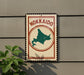 A sign with the word "Hokkaido" on it, featuring a map of the island, is mounted on a wall next to a plant.