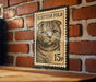 A wooden table with a brick wall in the background, and a framed Scottish Fold cat stamp on the wall.