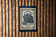 A black and white illustration of a basket filled with yarn and knitting needles is displayed on a wooden wall.