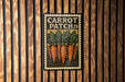 A vintage-style metal sign with the text "CARROT PATCH 29" and an illustration of several carrots growing in a patch of soil.
