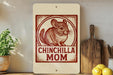 A sign with a chinchilla illustration and the text "CHINCHILLA MOM" is displayed on a shelf next to a wooden cutting board and some kitchen utensils.