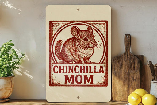 A sign with a chinchilla illustration and the text "CHINCHILLA MOM" is displayed on a shelf next to a wooden cutting board and some kitchen utensils.