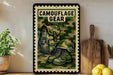 A framed poster with a camouflage design, featuring a backpack and boots, is displayed on a shelf next to a wooden cutting board and a potted plant.