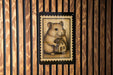 A wooden wall with a framed illustration of a hamster holding a small house.