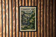 A poster with a camouflage pattern and a backpack is displayed on a wooden wall.