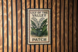 A metal sign with the text "LILY OF THE VALLEY PATCH" is displayed on a wooden wall.