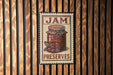 A vintage-style metal sign with the text "JAM PRESERVES" and an illustration of a jar of jam, mounted on a wooden wall.