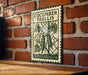 A metal sign with the text "CUCUMBER TRELLIS" is hanging on a brick wall, with a wooden table below it.