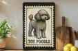A framed illustration of a toy poodle is displayed on a shelf, accompanied by a wooden cutting board, a potted plant, and some lemons.