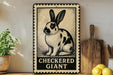 A decorative metal sign featuring a black and white illustration of a rabbit, with the text "CHECKERED GIANT" below it. The sign is placed on a wooden shelf, with a potted plant, a wooden cutting board, and some lemons nearby.