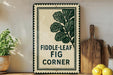 a sign with the text "FIDDLE-LEAF FIG CORNER" and a decorative leaf design, placed on a shelf next to a wooden cutting board and some potted plants.