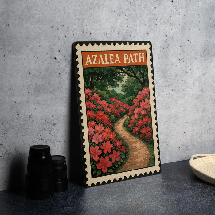 A framed print of a garden path with red flowers is displayed on a table, with a stack of black camera lenses and a white dish nearby.