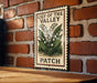 A vintage-style sign for a "Lily of the Valley Patch" is displayed on a brick wall, featuring an illustration of lily of the valley flowers.