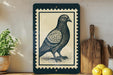 a framed illustration of a pigeon on a wooden surface, with a potted plant and a wooden cutting board visible in the background.
