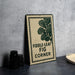 a sign with the text "Fiddle-leaf Fig Corner" on it, placed on a countertop next to some black camera lenses.