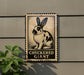 A sign featuring a cartoon rabbit with large ears, mounted on a wall next to a plant.