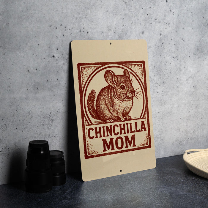 A sign with a chinchilla illustration and the text "CHINCHILLA MOM" on it, placed on a countertop next to some black camera lenses.