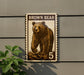 A brown bear stamp with the number 5 on it, mounted on a wall next to a plant.