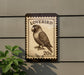 A postage stamp-like sign featuring a parrot, mounted on a wall next to a plant.