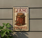 A vintage-style metal sign with the text "JAM PRESERVES" and an illustration of a jar of jam, mounted on a wall next to a plant.