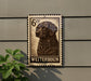 A metal sign with a stamp-like design featuring a dog's head, mounted on a wall next to a plant.