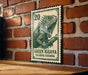 A green and white postage stamp featuring a detailed illustration of a green iguana is displayed on a brick wall.