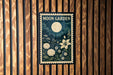 A framed poster with a moon and floral design hangs on a wooden wall.