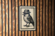 A black and white illustration of a bird wearing a hat is displayed on a wooden wall.