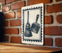 A sign with a black and white illustration of a broom and a dustpan is mounted on a brick wall.