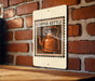 A copper kettle illustration on a sign is displayed against a brick wall.