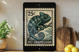 A 25c postage stamp featuring a chameleon is displayed on a shelf next to a wooden cutting board and some lemons.