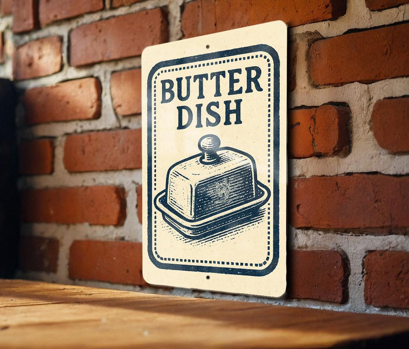 A sign with the word "BUTTER DISH" on it, featuring an illustration of a butter dish, is mounted on a brick wall.