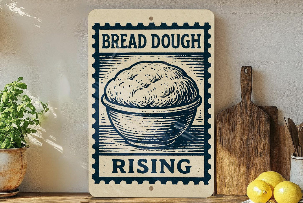 a sign that reads "BREAD DOUGH RISING" with a picture of a bowl of dough on it. The sign is placed on a wooden surface, and there are some kitchen utensils, such as a knife and a spoon, visible in the background.