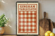 A vintage-style sign for "Gingham Tablecloth" is displayed on a shelf, accompanied by a wooden cutting board, a potted plant, and some lemons.