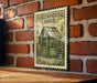 A metal sign with a green border and a drawing of a greenhouse is mounted on a brick wall.