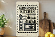 a sign that reads "Farmhouse Kitchen" with various kitchen items such as pots, pans, and utensils depicted on it. The sign is displayed on a wall next to a wooden cutting board and a potted plant.