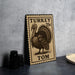 A wooden postcard featuring a turkey stamp with the text "TURKEY 25c TOM" printed on it, placed on a table next to some black camera lenses.