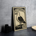 A metal stamp with a bird illustration and text, placed on a table next to some black camera lenses.