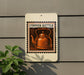 a copper kettle on a white sign with a black border, mounted on a gray wall.