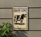 a sign with a cow illustration, mounted on a wall.
