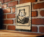 A metal sign featuring a cartoon image of a hamster sitting on a laptop computer, mounted on a brick wall.