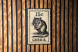 A postage stamp featuring a small rodent, likely a rat, is displayed on a wooden background.