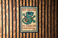 A vintage-style metal sign with a gecko wearing sunglasses and the text "MY GECKO IS COOLER THAN YOUR 15¢" is displayed on a wooden wall.