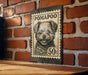 A black and white postage stamp featuring a dog's face is mounted on a brick wall.