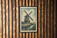A framed illustration of a windmill is displayed on a wooden wall.