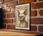 A framed image of a Sphynx cat is displayed on a brick wall.