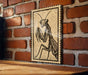 a wooden table with a framed illustration of a praying mantis on it, mounted on a brick wall.
