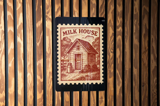 A wooden wall with a red and white postage stamp featuring a small house and a cow, mounted on the wall.