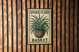 A sign with a spider plant and a basket, mounted on a wooden wall.